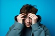 Medium shot portrait photography of a glad boy in his 20s covering one's eyes against a cerulean blue background. With generative AI technology