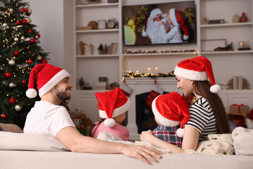 Canvas Print - Happy family wearing Christmas hats spending time near TV in cosy room. Winter holidays atmosphere