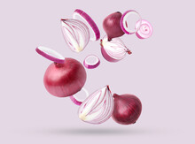 Whole and cut fresh red onions falling on light violet background