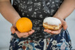 osoba trzymająca pączka i pomarańcz w dłoniach