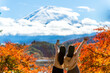 Happy Asian woman travel Japan on holiday vacation. Attractive girl friends using mobile phone taking selfie together while travel Mt.Fuji and looking beautiful red maple tree leaf falling in autumn