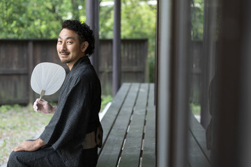 Wall Mural - うちわをもって縁側でくつろぐ浴衣の日本人男性 夏の旅館や旅行のイメージに　