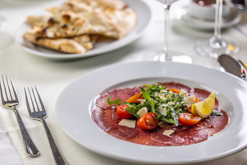 Wall Mural - Typical Italian appetizer, carpaccio from veal or beef thinly sliced and served on a plate with salad