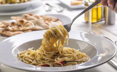 Wall Mural - Hand with a fork spinning spaghetti aglio e olio peperoncino from a plate in a restaurant