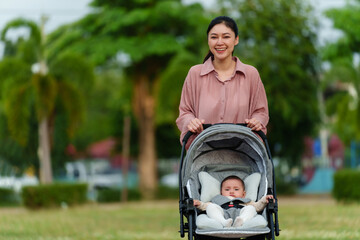 Wall Mural - happy mother pushing infant baby stroller and walking in park