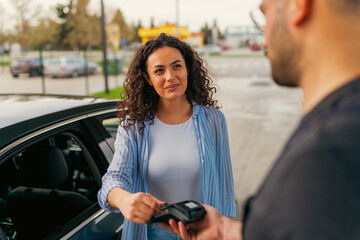 A young woman pays for fuel at a gas station using a card, the worker gave her a terminal to pay