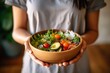 © sirisakboakaew - Healthy salad bowls held by Asian women in gym clothes to promote good health and wellness at home.;Generated with AI