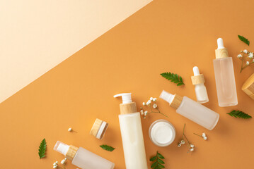 Organic cosmetic products concept. Top view photo of cosmetic jars, bottles and tubes, fern leaves and white gypsophila flowers on isolated beige and brown background with copyspace