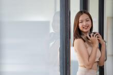 Young Beautiful Asian Woman With Headphone On Neck And Standing Near A Window.