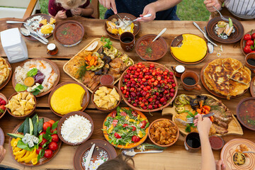 Homemade Romanian Food with grilled meat, polenta and vegetables Platter on camping. Top view of group of people having dinner together on wooden table in garden.