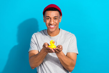 Sticker - Photo of funny cheerful guy dressed grey t-shirt holding arms yellow rubber duck isolated blue color background