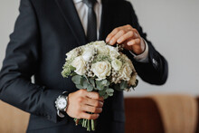 Portrait. A Man In A White Shirt, Black Bow Tie And Black Tie Poses In A Room With A Wedding Bouquet. A Stylish Watch. Men's Style. Fashion. Business