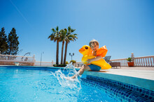 Boy At Resort Pool Enjoys Summer, Splashing In Buoy And Floaties