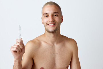 Perfect smile. Portrait of handsome young man posing shirtless with toothbrush against white studio background. Concept of men's beauty, skincare, dental teeth care, health. Copy space for ad