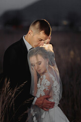 Wall Mural - Beautiful bride and groom in evening lights, kissing and hugging holding a bouquet of flowers