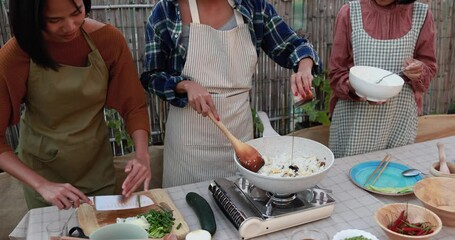 Wall Mural - Happy asian mother and adult daughters preparing together traditional thai food at house backyard - Adult daughter adding soy sauce to the rice