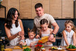 © dvulikaia - Young parents teach their little daughters to cook vegetarian salad at the kitchen.
