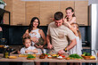 © dvulikaia - A large family - mom, dad, three daughters and a baby son together prepare a salad for lunch in a modern kitchen. Big family together concept.
