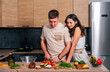 © dvulikaia - Young man cooking salad at the kitchen and his happy wife hugging him.