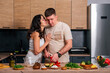 © dvulikaia - Young man cooking salad at the kitchen and his happy wife hugging him.