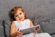 © dvulikaia - Happy little child sitting on sofa and using tablet.