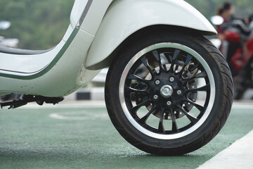 Close-up of wheels of a scooter motorcycle parked on a beautiful road in the daytime.