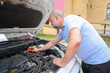 © Olga - A bearded man leaned over the open hood of a black car with a screwdriver during the repair process.