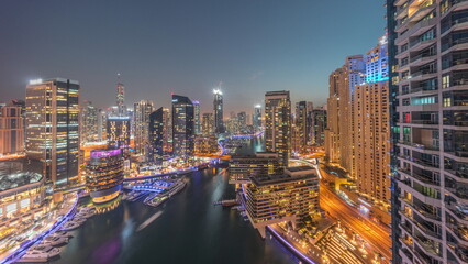 Aerial view to Dubai marina skyscrapers around canal with floating boats day to night timelapse