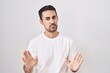 Handsome hispanic man standing over white background moving away hands palms showing refusal and denial with afraid and disgusting expression. stop and forbidden.