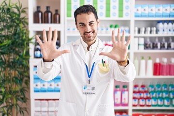 Sticker - Handsome hispanic man working at pharmacy drugstore showing and pointing up with fingers number ten while smiling confident and happy.