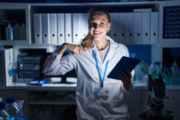 Wall Mural - Beautiful blonde woman working at scientist laboratory late at night looking confident with smile on face, pointing oneself with fingers proud and happy.