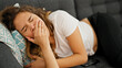 Young beautiful hispanic woman lying on sofa yawning at home