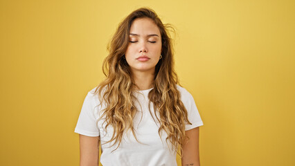 Young beautiful hispanic woman standing with serious expression and close eyes over isolated yellow background