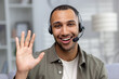 © Tetiana - Close-up photo. Face portrait of a smiling young African American man at home wearing a headset talking and greeting the camera