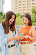© Jose Calsina - Vertical. Two cheerful smiling women watching and showing sale, news and social media on their smartphone app outside at the university campus. Young teenage females using a cellphone together. High