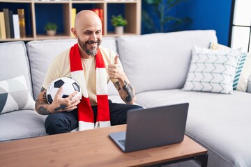 Poster - Hispanic man with tattoos watching football match hooligan holding ball on the laptop smiling happy and positive, thumb up doing excellent and approval sign