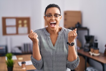 Canvas Print - African american woman working at the office wearing glasses celebrating surprised and amazed for success with arms raised and open eyes. winner concept.