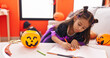 © Krakenimages.com - Adorable hispanic girl drawing on notebook having halloween party at home