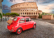 Little red old Fiat 500 in front of coliseum at sunset with picnic basket on rear