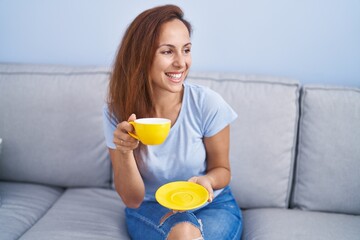 Sticker - Young woman drinking coffee sitting on sofa at home