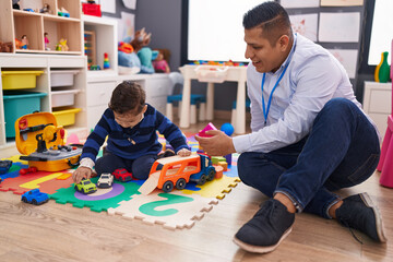 hispanic man and boy playing with car toy sitting on floor at kindergarten