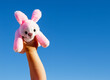 Child arm holding up a pink bunny against blue sky.