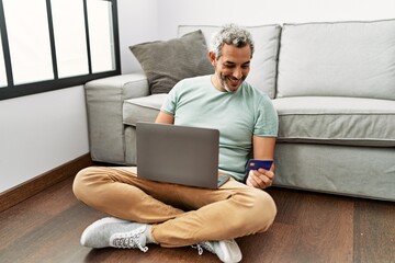 Sticker - Middle age grey-haired man using laptop and credit card sitting on floor at home