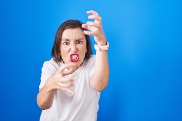 Poster - Middle age hispanic woman standing over blue background shouting frustrated with rage, hands trying to strangle, yelling mad