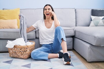 Sticker - Young brunette woman doing laundry at home angry and mad screaming frustrated and furious, shouting with anger looking up.