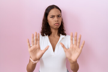 Young hispanic woman wearing casual white t shirt moving away hands palms showing refusal and denial with afraid and disgusting expression. stop and forbidden.