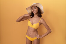 Young Hispanic Woman Wearing Bikini And Summer Hat Smiling Doing Phone Gesture With Hand And Fingers Like Talking On The Telephone. Communicating Concepts.