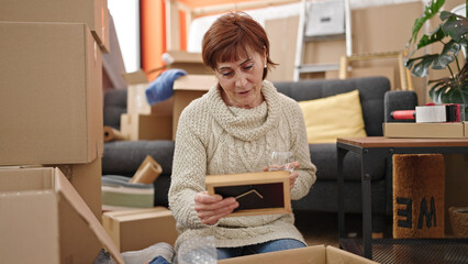 Wall Mural - Mature hispanic woman unpacking cardboard box drinking wine at new home