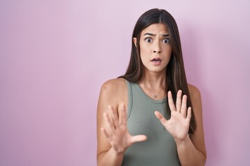 Sticker - Hispanic woman standing over pink background afraid and terrified with fear expression stop gesture with hands, shouting in shock. panic concept.