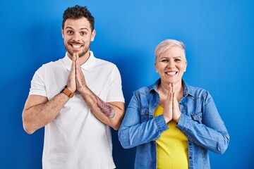 Sticker - Young brazilian mother and son standing over blue background praying with hands together asking for forgiveness smiling confident.